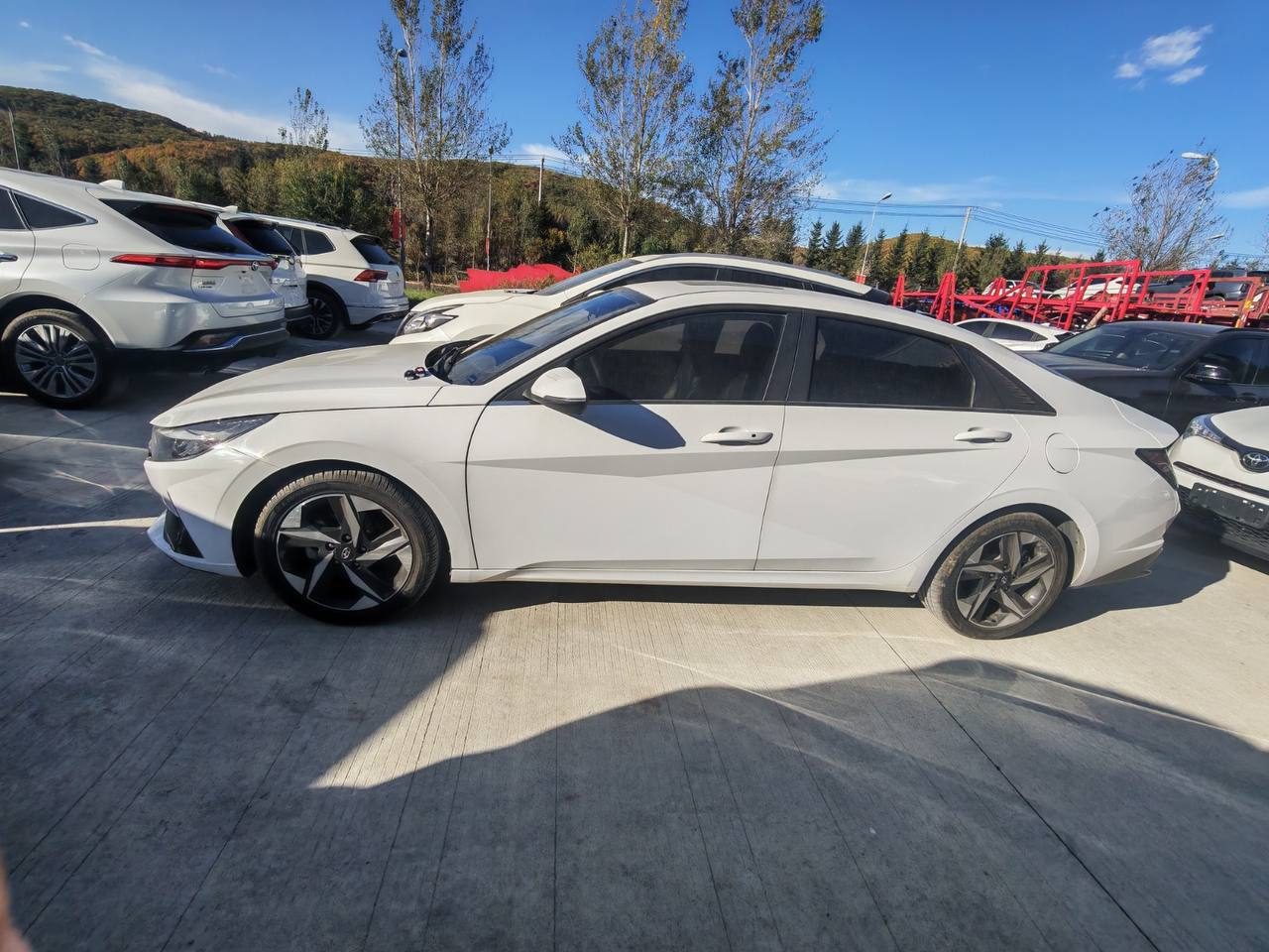 Белый седан Hyundai на экспортной площадке среди других автомобилей